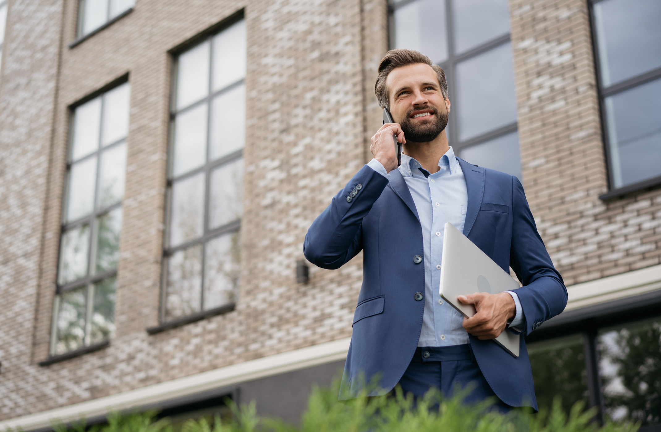 real estate investor standing in front of a property with a phone and laptop